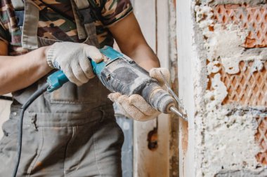 Pnömatik çekiç delici ve elmas kaplama delgisi olan tamirci elektrik kablosu, soket, anahtar için duvarda delik açıyor.