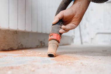 Beton duvarı deldikten sonra zemindeki kalıntıları ve tozu süpüren bir işçi.