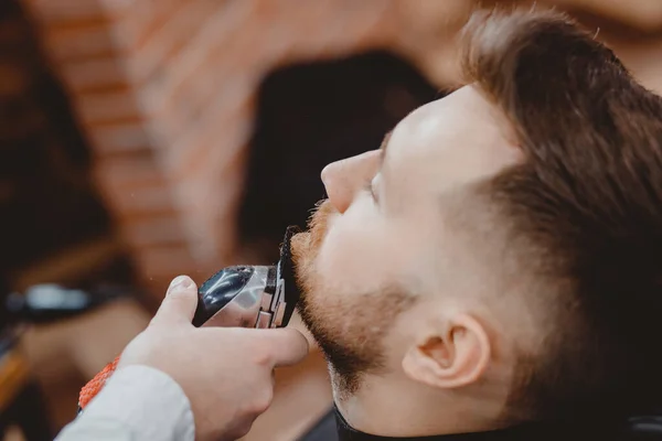 Barber scheren baard aan man in kapperszaak inlijsten haarlijn. elektrisch scheermes, vintage getint bruin — Stockfoto