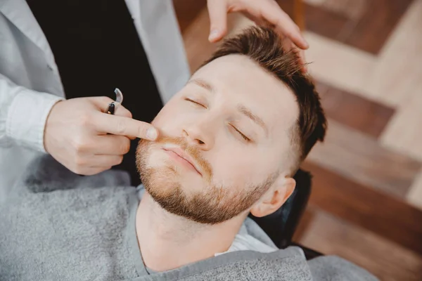 理发师把泡沫和胡子剃须乳液涂在男性客户身上。乳脂及油类护肤概念 — 图库照片