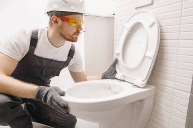 Tesisatçı tuvalete klozet yerleştiriyor, banyoda çalışıyor.