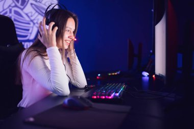 Flamalı güzel kız profesyonel oyuncu kulaklıklı, kırmızı ve mavi renkli online oyun bilgisayarı oynuyor.
