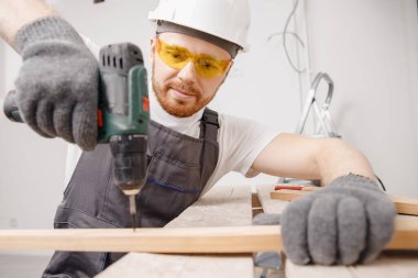 İşçi marangoz elektrikli tornavidayla tahta tahtaya metal vidaladı.