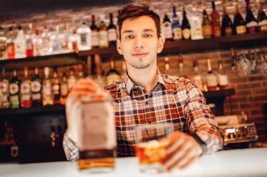 Barmen şişeden bardağa viski doldurur. Koyu kahverengi arkaplan