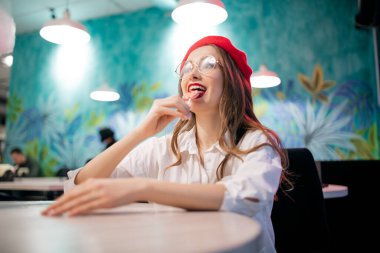 Kız Fransa 'da kafeteryada lolipop şekeri yiyor, genç kadın kırmızı bereli ve gözlüklü.