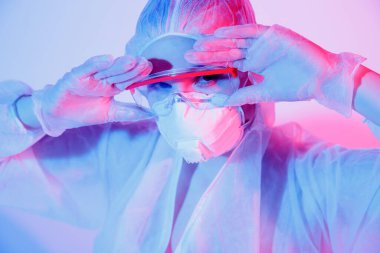 Salgınlara karşı koronavirüs koruması. Koruyucu giysili genç kadın, tıbbi maske ve pembe ve mavi arka planda gözlük.