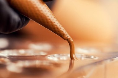 Şef ya da çikolatacı eritilmiş siyah çikolatayı pasta poşetinin üzerine silikon kalıplara döküyor.