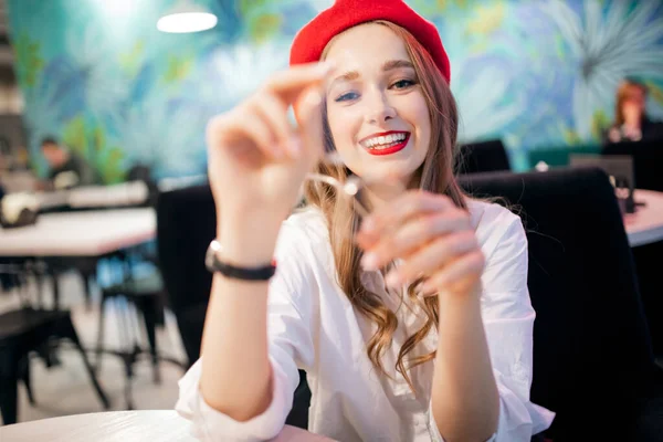 Die junge schöne Französin mit der roten Baskenmütze in einem Café zeigt eine Brille. Zahn- und Augengesundheitskonzept — Stockfoto