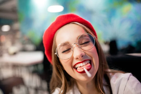 Menina comendo pau pegajoso doce na França café em boina vermelha e óculos. Cárie conceito e dano é perigo para o esmalte dentário — Fotografia de Stock