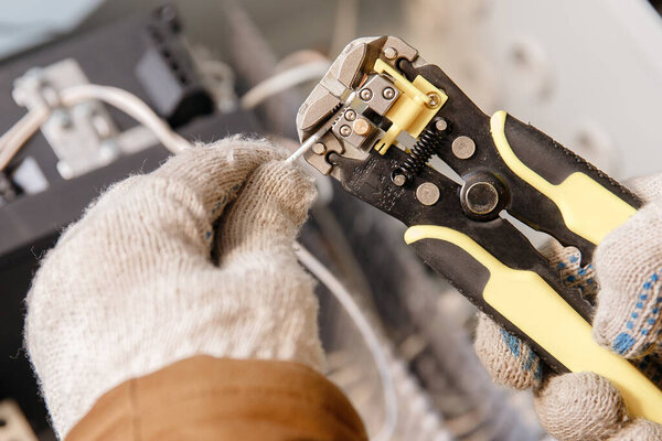 Master electrician with professional tool for removing insulation from power cable, installing networks