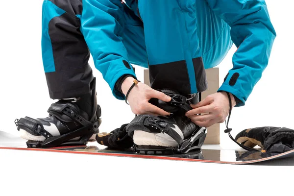 Ritratto giovane uomo in abbigliamento sportivo con snowboard fissa stivali isolato sfondo bianco — Foto Stock