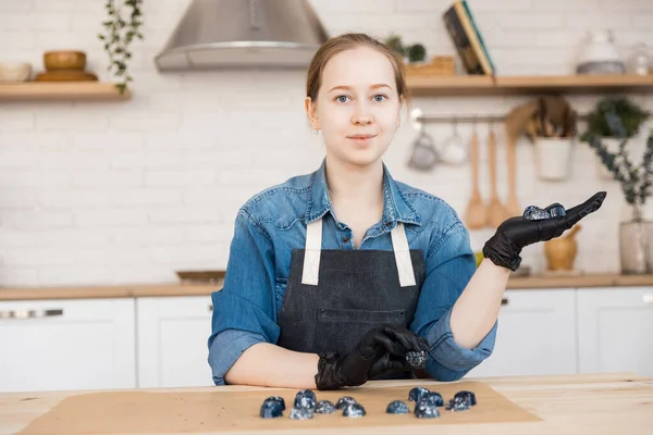 Retrato de mulher jovem empresária segurando cozinheiro de chocolates no fundo da cozinha. Conceito pequena empresa pastelaria chef casa — Fotografia de Stock