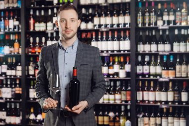 Sommelier 'ın adamı arka plandaki restoranda şişe kırmızı şarap ve cam tutuyor.