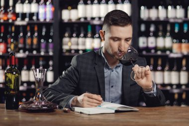 Sommeliers erkeği kırmızı şarabı tadıyor ve aroma degukasyonu kartı yazıyor.