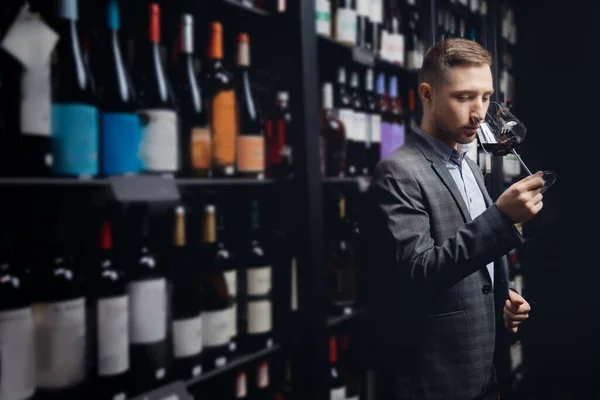 Sommelier man holds glass with red wine in restaurant, tests aroma and color