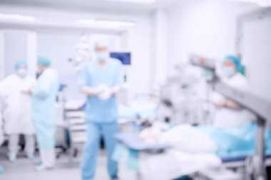 Ameliyat odasının geçmişi bulanık, hasta masada yatıyor, doktorlar çalışıyor.