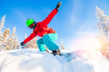 Aktif snowboardcu, güneşli bir günde dağlarda yamaçta at sürüyor. Tozlu kar ormanı