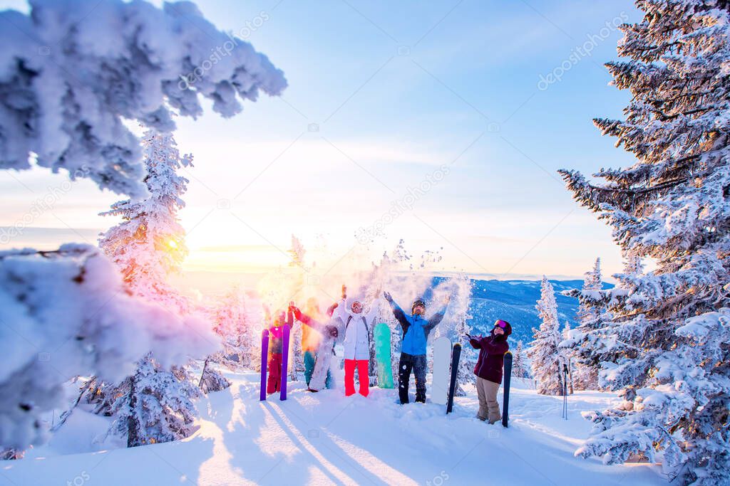Happy team of snowboarders and skier having fun tossing snow. Light sun in winter forest sunrise