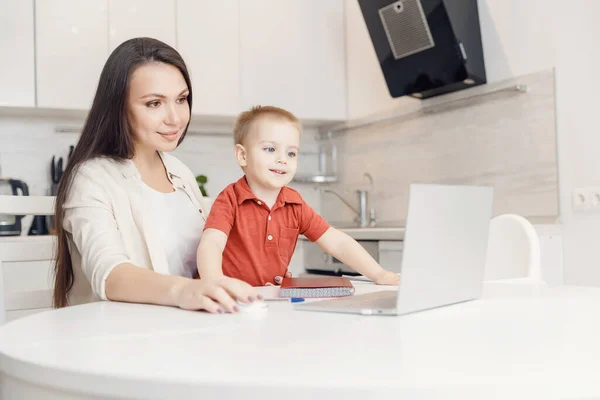 Kobieta na urlopie macierzyńskim pracuje w domu online z laptopem w kuchni z małym dzieckiem. Concept mama praca podczas kwarantanny izolacji podczas Covid-19 — Zdjęcie stockowe