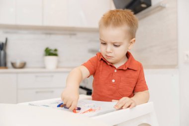 Çocuk kalemle çizmeyi kâğıt evde, beyaz mutfak arka planında öğreniyor.