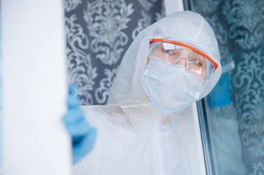 Yalnızlık karantinası, tıbbi maskeli genç bir kadın pencereden kendini izole ediyor. Coronavirüs salgını konsepti