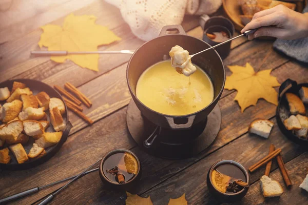 Mädchen kocht Schweizer Gourmet-Fondue-Abendessen mit Käse auf Feuer, Herbst-Holzhintergrund mit Ahornblättern. Draufsicht, flache Lage — Stockfoto