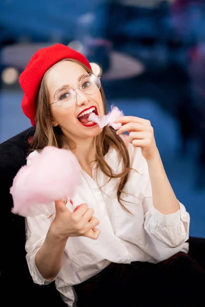 Молода дівчина в червоному береті і окуляри їдять рожеві цукерки в кафе Франції. — стокове фото