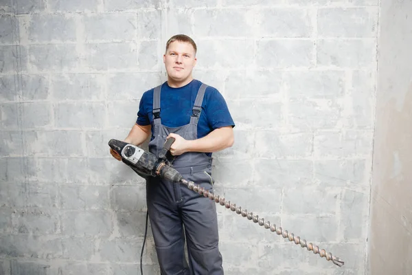 Hombre trabajador constructor sostiene gran taladro fondo gris pared — Foto de Stock