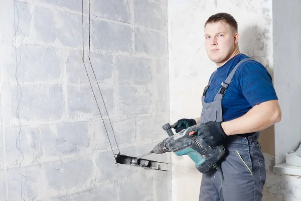 Constructor trabajador hombre utilizando martillo neumático para perforar en la pared de construcción para conducto para tubos de aire acondicionado — Foto de Stock