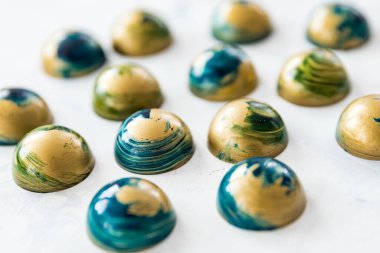 Yakın plan çikolatalı şekerler mavi ve altın rengi kalp şeklinde, taşın altında beyaz lekeler var.