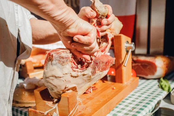 Male butcher cuts dried pork leg prosciutto ham with knife in center of Rome. Italy