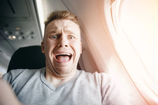 Pasajero masculino en avión grita y llora, aerofobia. fondo de ojo de buey. Concepto miedo a volar en avión — Foto de Stock