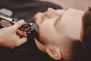 Berber adam berber dükkanında müşterisinin sakalını kesiyor.