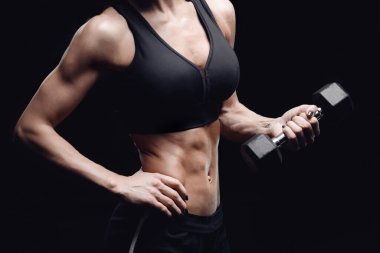 Fitness konsepti, egzersiz. Ayrı siyah arka planda, elinde dambıllar olan genç bir kadın.