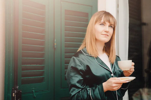 Belle jeune femme avec tasse café sur terrasse en pyjama vert rencontre le matin — Photo