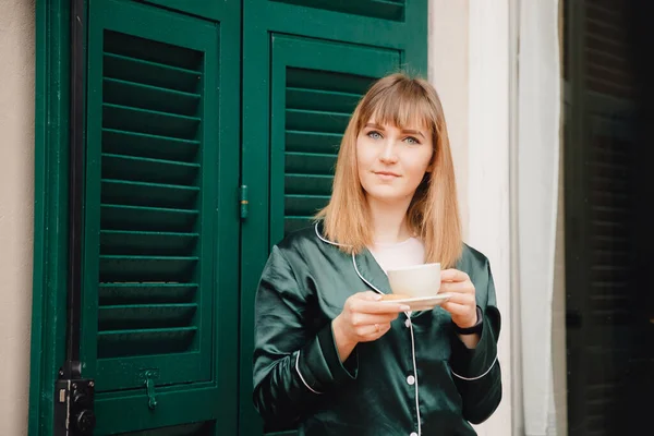 Belle jeune femme avec tasse café sur terrasse en pyjama vert rencontre le matin — Photo