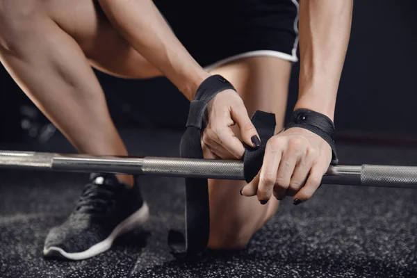 Jonge vrouw handen doen riemen om haar polsen voor lange halter verzekering sportschool. Workout concept — Stockfoto