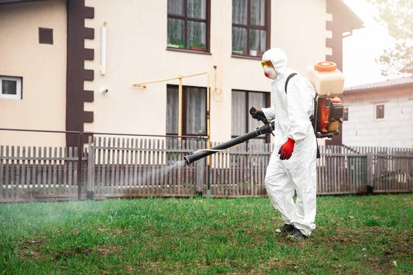 Disinfector in protective suit processes territory of garden plot of house sprays poison from mosquitoes, ticks and pests — Stock Photo, Image