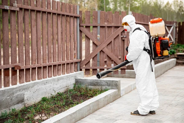 Disinfector in protective suit processes territory of garden plot of house sprays poison from mosquitoes, ticks and pests — Stock Photo, Image