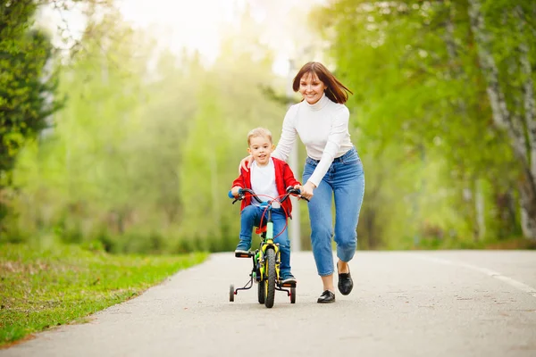 Menino aprende a andar de bicicleta, sua mãe está feliz e ri sucesso. Conceito família, apoio — Fotografia de Stock