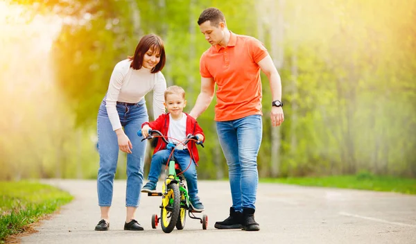 Pai feliz e mãe ensinando seu filho a andar de bicicleta. Atividades familiares dia de verão — Fotografia de Stock