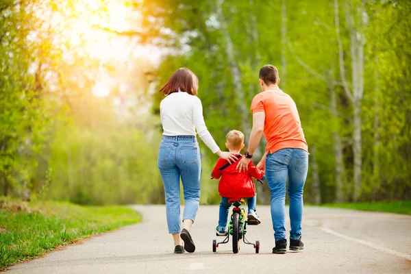 Pai e mãe ensina o filho a andar de bicicleta no parque, se divertir com a família, vista para trás — Fotografia de Stock