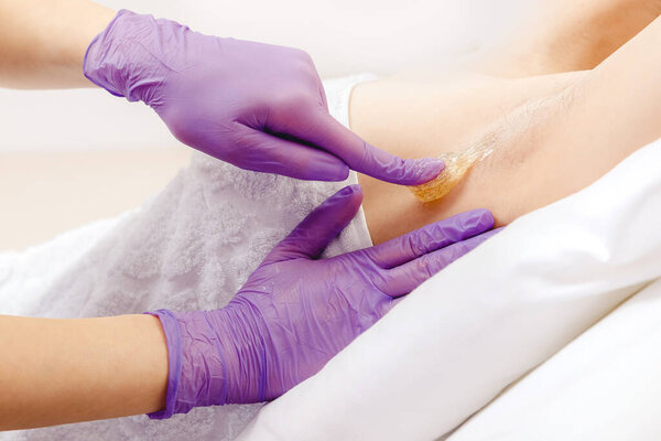 Master beautician removes hair from female underarm with sugar paste, white color. Sugaring beauty concept
