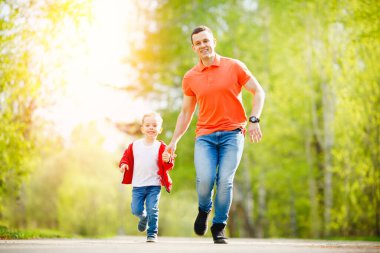 Baba ve oğul yaz parkında el ele koşarlar. Mutlu aile kavramı