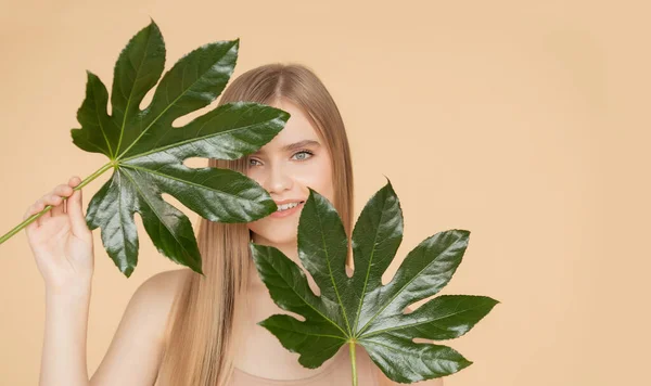 Έννοια φυσικών καλλυντικών για το δέρμα του προσώπου, τα φρύδια και τα μαλλιά. Πορτρέτο γυναίκα με πράσινο φύλλο, ξανθιά μοντέλο κορίτσι με χαμόγελο — Φωτογραφία Αρχείου
