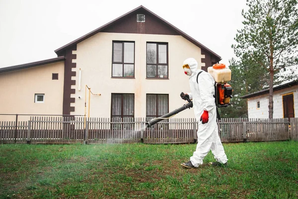 El desinfectador en el traje protector procesa el territorio de la parcela de jardín de la casa rocía el veneno de los mosquitos, las garrapatas y las plagas — Foto de Stock