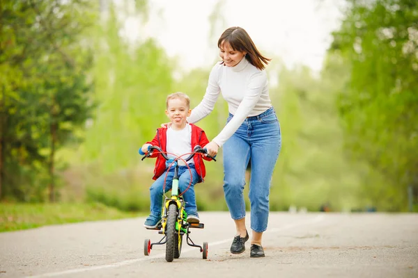 Kleine jongen leert fietsen, zijn moeder is gelukkig en lacht om succes. Concept familie, ondersteuning Rechtenvrije Stockfoto's