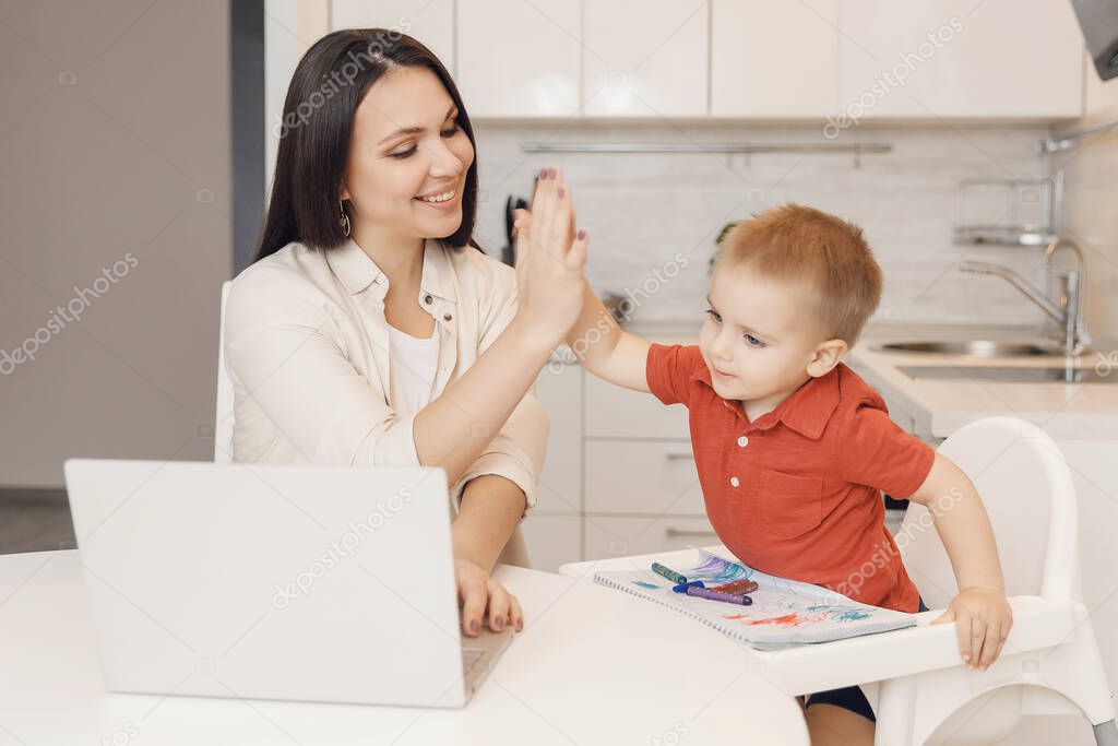 Mom with her son rejoices success of table in kitchen with laptop makes gesture to give five with palm. Concept training, spending time together