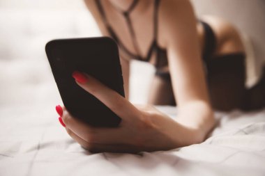 Güzel bir kadın, erkek için telefonda iç çamaşırlarıyla fotoğraf çekiyor. Sanal seks modeli konsepti