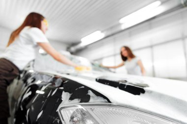 Arka plan bulanık. Beyaz köpüğü yıkamak için siyah arabanın üzerinde sünger var.